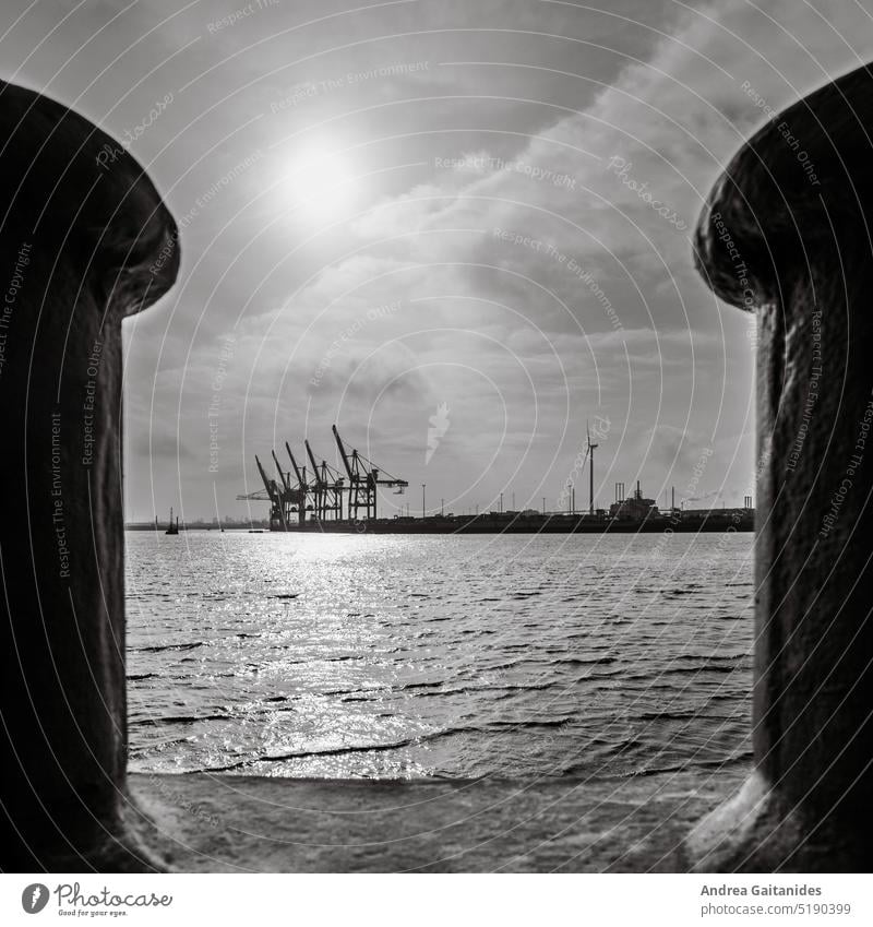 View through two bollards at the port of Hamburg on harbor cranes, water and sky, 1:1, square , black and white Bollard view through Between Harbour
