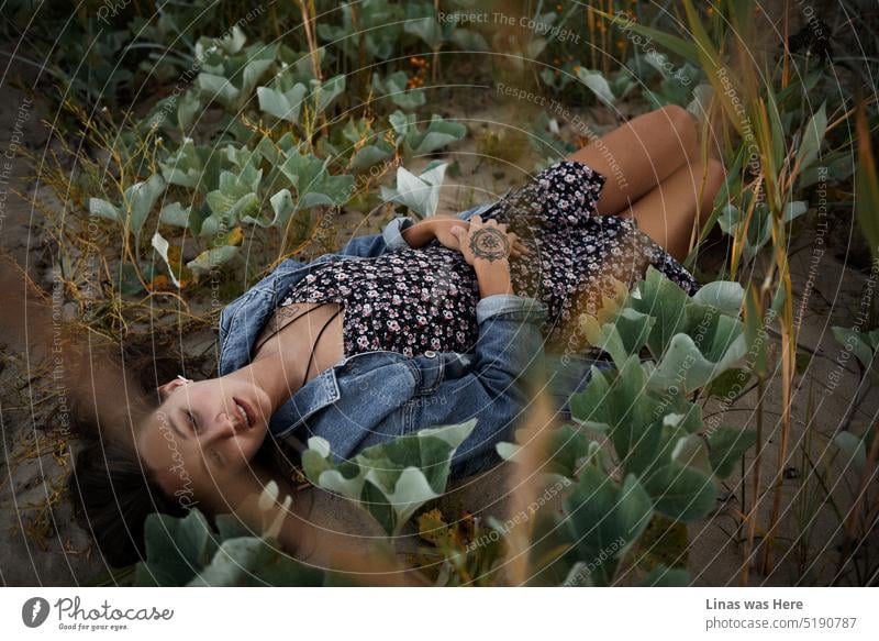 Here is a lying beauty on these wildflowers and dunes sand. Her tanned skin, dark hair, and pretty face match perfectly this beauty in nature that surrounds her comfortably. Enjoy, relax, and let your worries float away.