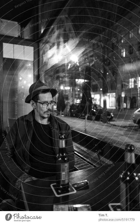 Man with hat and glasses at a table in a bar Hat Eyeglasses Night Window Facial hair Prenzlauer Berg Autumn chestnut avenue b/w bnw Black & white photo Town