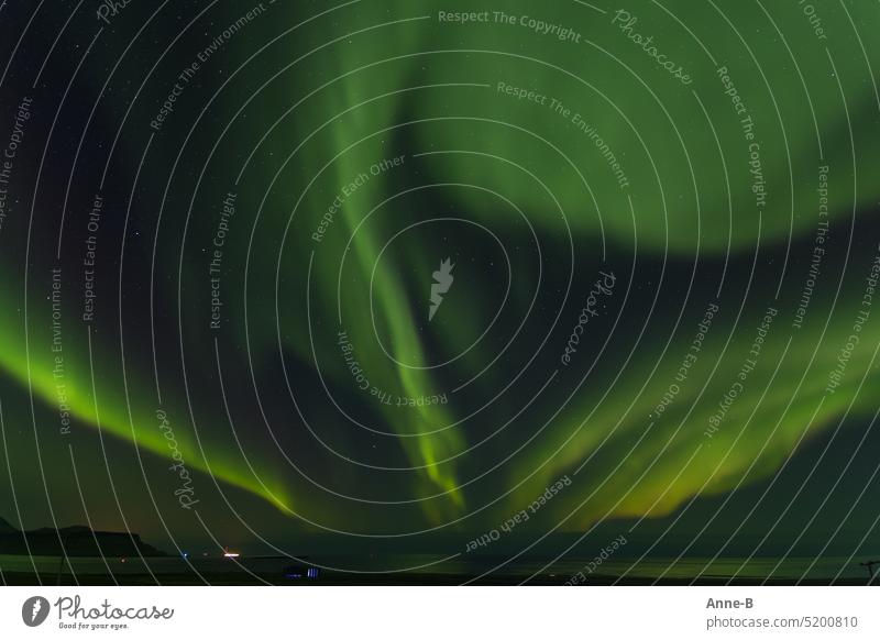 Northern lights over the fjord, it looks like a big green flower. At the fjord is a hangar from which blue light seeps. Aurora Borealis Green aurora polaris