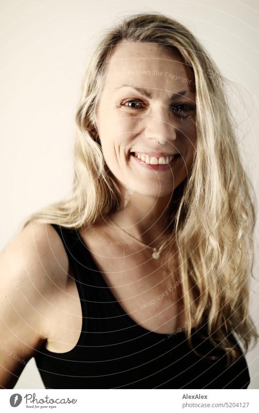 side portrait of blonde long haired woman in black tank top Woman Blonde Long-haired Smiling Looking into the camera Slim daintily pretty naturally Emanation