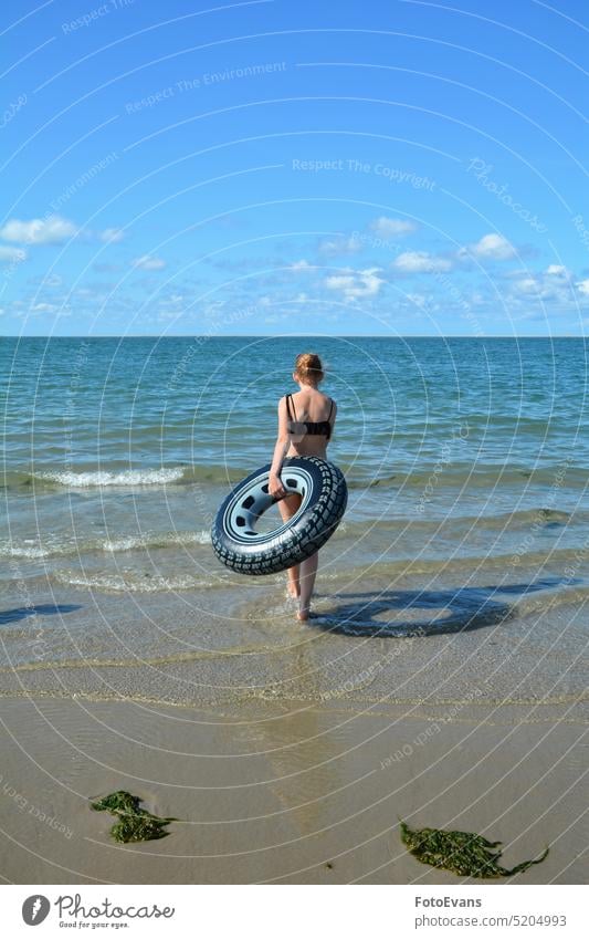 Young girl from behind, with a swimming tire runs into the sea on a sandy beach Girl Beach voyage holidays Vacation & Travel coast Tourism Landscape Ocean