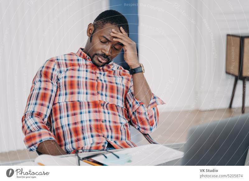 Tired african american male employee suffering from headache after working at laptop. Stress at work man fatigue tired stress hurt burnout migraine sleepy