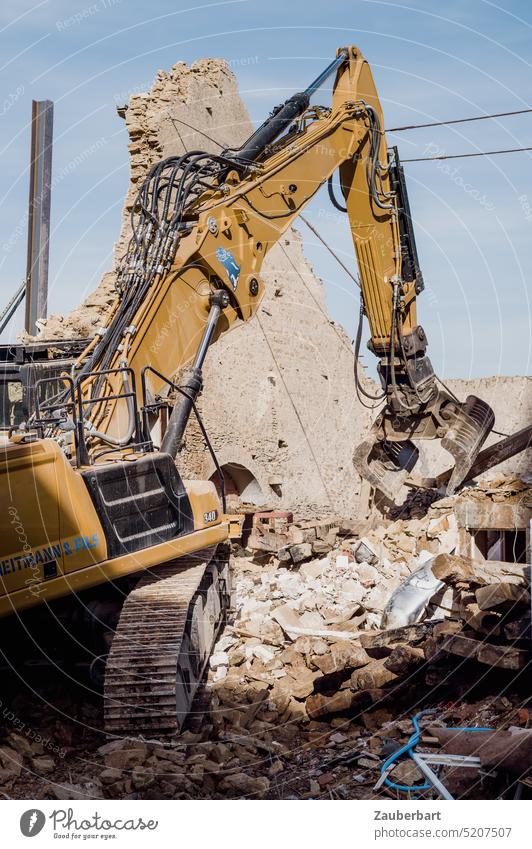 Yellow excavator demolishes a historic house, of which only the gable wall remains Excavator Crawler excavator Construction machinery