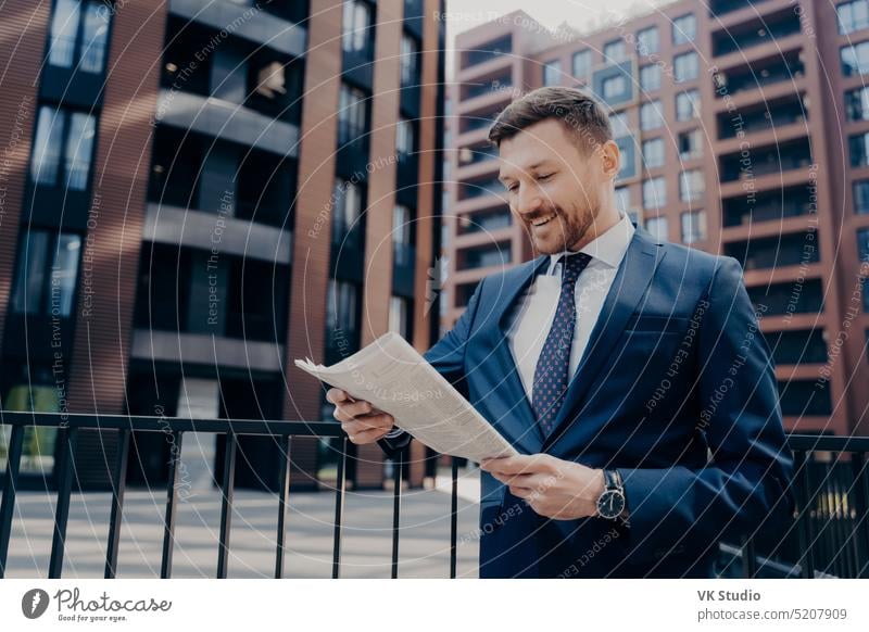 Successful happy young male economist reading article with financial news in morning newspaper successful smiling businessman stylish suit about corporate