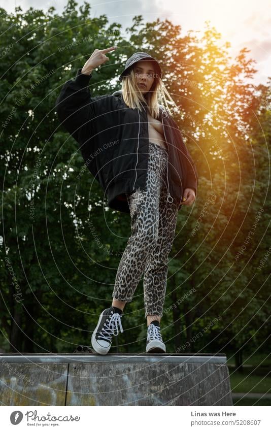 A fashionable and sexy skater girl is having some fun in a skate park. Being almost topless. Showing middle finger. Just being a wild fashionista. A pretty blonde girl is feeling free and enjoying just being herself.