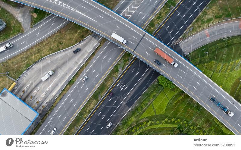 Aerial top view of highway junction interchange road. Drone view of the elevated road, traffic junctions, and green garden. Transport trucks and cars driving on highway. Infrastructure in modern city.