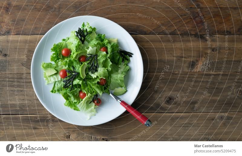 White plate of mixed salad with seaweed, tomatoes, lettuce and avocado. Wood background. Copy space. wooden bottom fork cutlery white plate salad plate