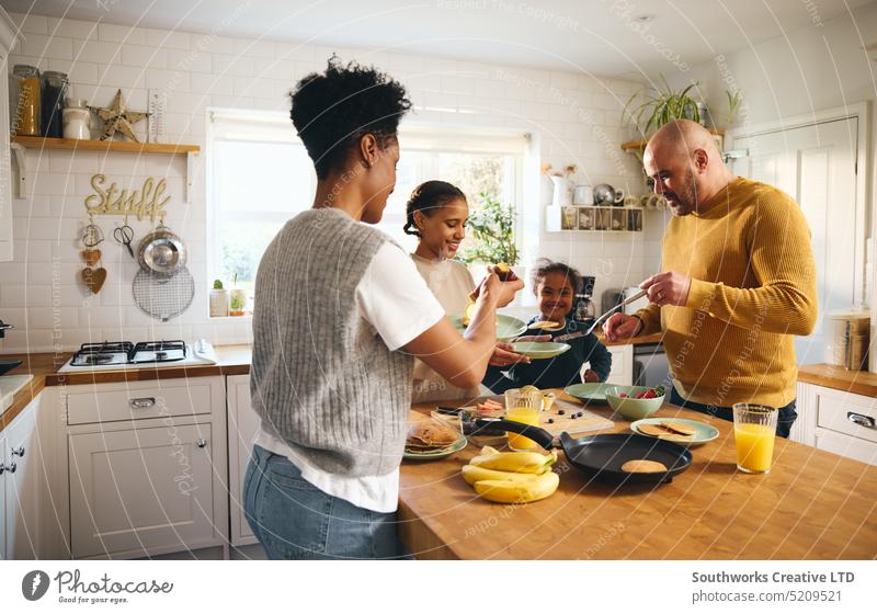 Family making pancakes for breakfast family boy down syndrome make parent four black kitchen food multiracial laugh joy fun worktop serve prepare meal