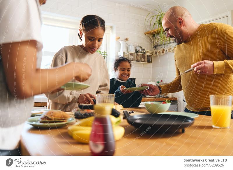 Family and boy with Down syndrome serving pancakes for breakfast family eat down syndrome serve parent four black kitchen food multiracial make laugh joy fun