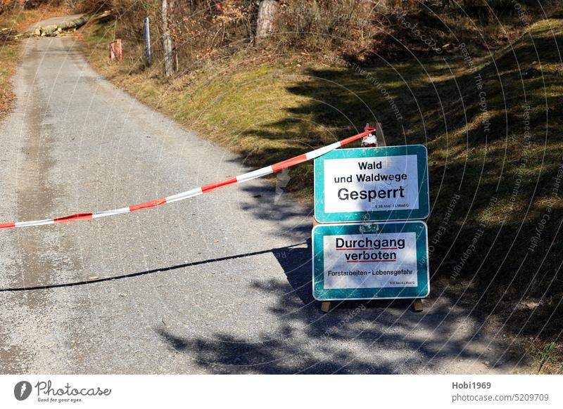 Forest road is closed for pedestrians by traffic signs and barrier tape forest path Road sign block cordon Barred Lumberjack Working man Tree off