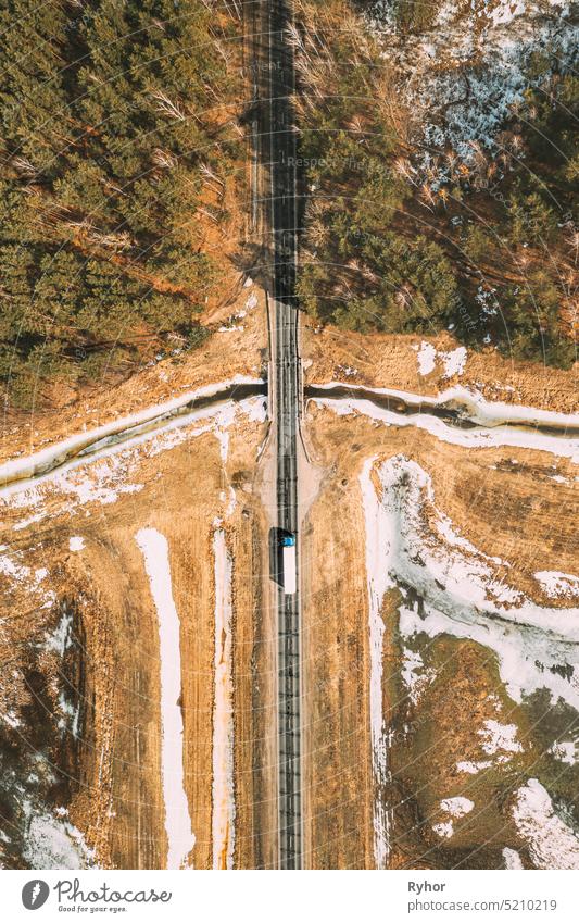 Aerial View Of Highway Road Through Spring Forest Landscape. Top View Of White Truck Tractor Unit Prime Mover Traction Unit In Motion On Freeway. Business Transportation, Trucking Industry. Flat View