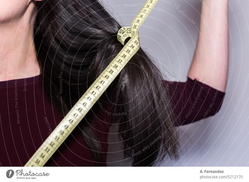 Woman holding a yellow measuring tape around a strand of her long hair. Hair and hairstyles Feminine Tape measure Measuring instrument Measure Measurement