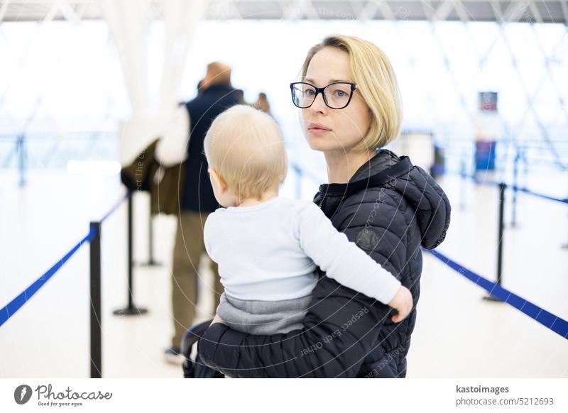Mother carying his infant baby boy child queuing at airport terminal in passport control line at immigrations departure before moving to boarding gates to board an airplane. Travel with baby concept.