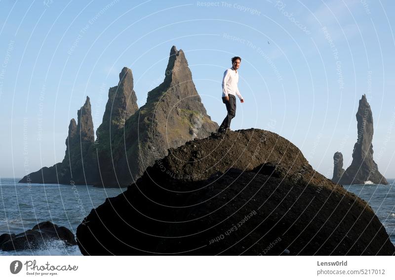 Man standing on a rock at Reynisfjara Black Beach, Iceland, with wind in his hair adventure black beach blue cliff concept freedom handsome hiking hill iceland