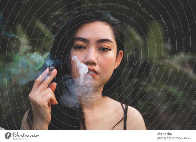 Yong Asia woman smoking at blur tree plant background addict adult art attractive beautiful beauty black cannabis caucasian cheerful cigarette colorful dark