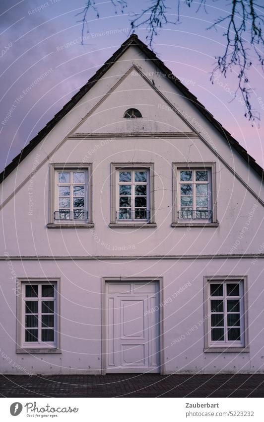 White gable end of old house with gable roof and muntin windows in purple colored evening light, symbolic for existing house, renovate and insulate pediment
