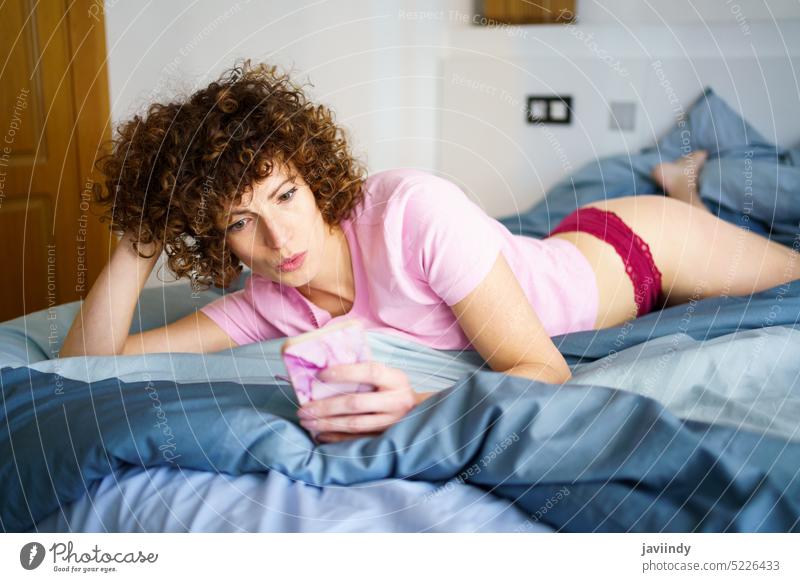 Charming woman text messaging on smartphone in bed using text message pouting lips comfort social media addict morning home bedroom gadget pretty curly hair