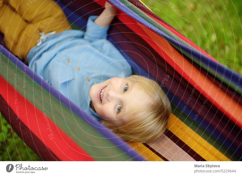 Cute little blond white boy enjoy and having fun with multicolored hammock in backyard or outdoor playground. Summer outdoors active leisure for kids. Child