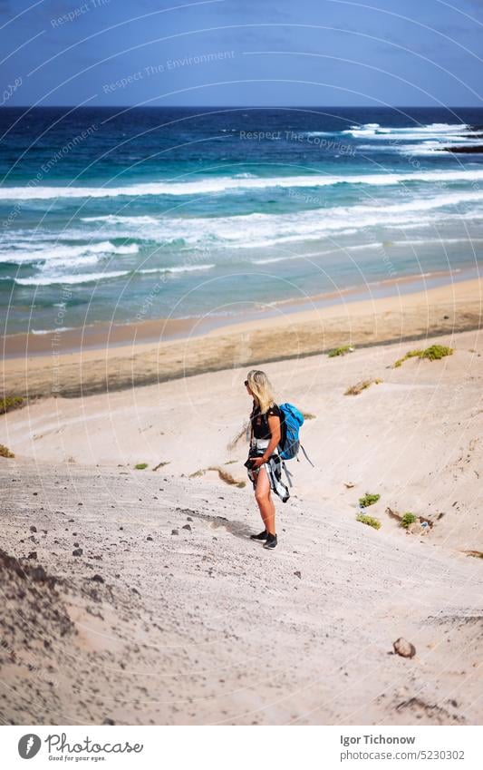 Woman hiker with backpack going down a sand dune towards the lonely beach. Sao Vicente Cape Verde sao vicente cape verde women beach female trekkers climbing