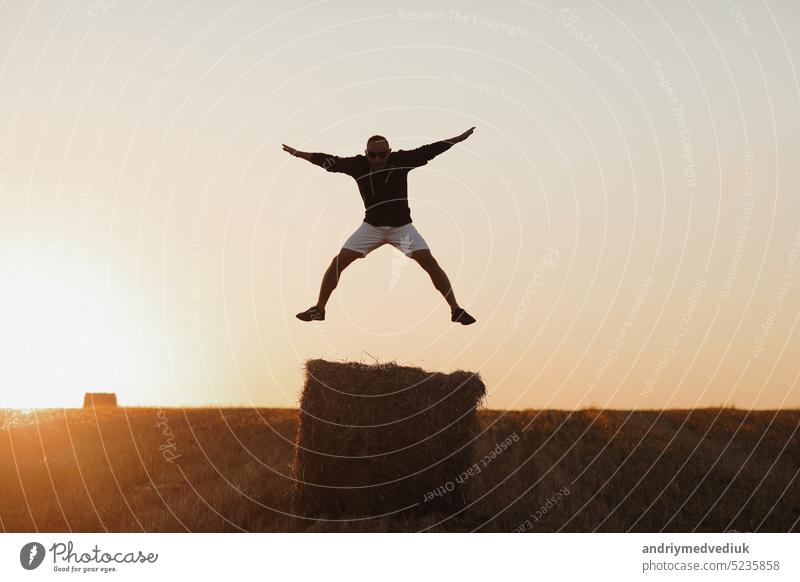 handsome young man in black sweatshirt and white short, in summer field outdoor, having fun on hay bale, haystack on sunset nature straw farm countryside people