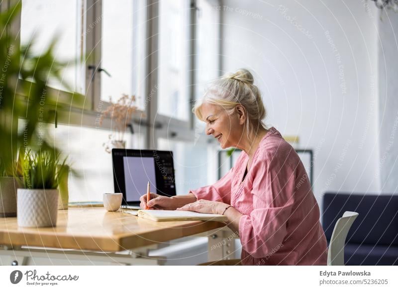 Woman sitting at desk, using computer and writing in notebook