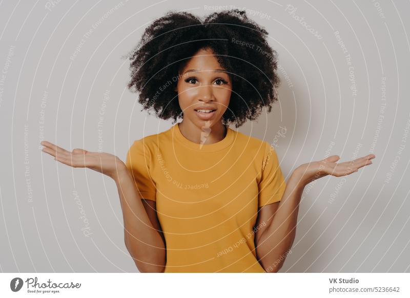 Confused doubtful black woman shrugging with shoulders, feeling baffled while looking at camera african american afro unaware confused expression hands clothes