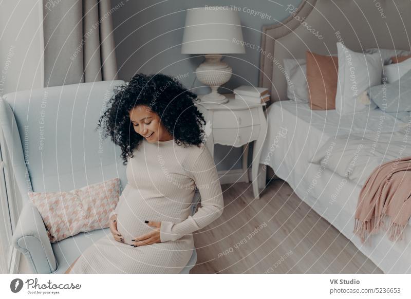 Pregnant caucasian woman resting at home. A young expectant mother reads a  doctor's report and looks at ultrasound pictures of her baby. Expectant mom  strokes her pregnant belly and thinks about baby 