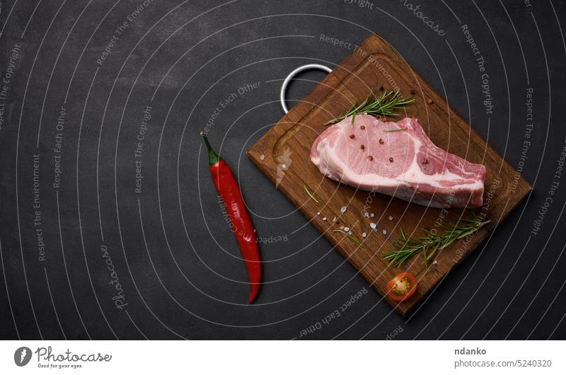 Raw pork tenderloin on the bone and spices on a wooden cutting board. Portion for lunch and dinner, top view. Copy space piece raw red rosemary salt barbecue