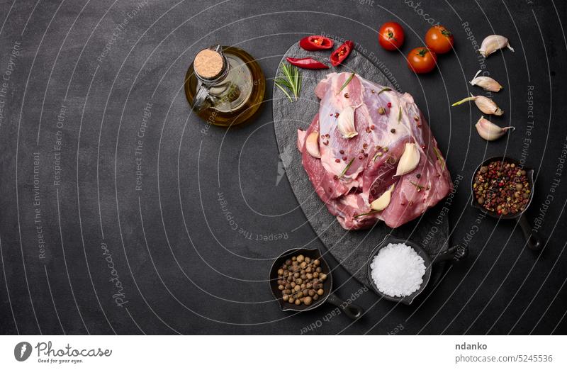 A piece of pork ham on a black board and spices olive oil, salt, rosemary branch and pepper garlic food slice butcher ingredient sirloin meal bottle raw part