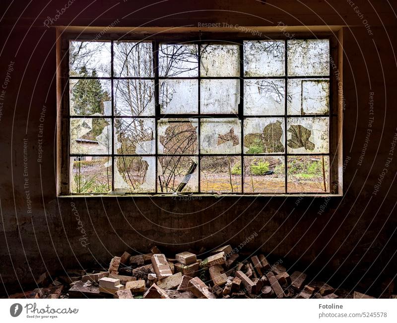Most of the window in this Lost Place is broken. Many panes of glass have been smashed. There is a pile of bricks under the window. Everything is broken and dirty.