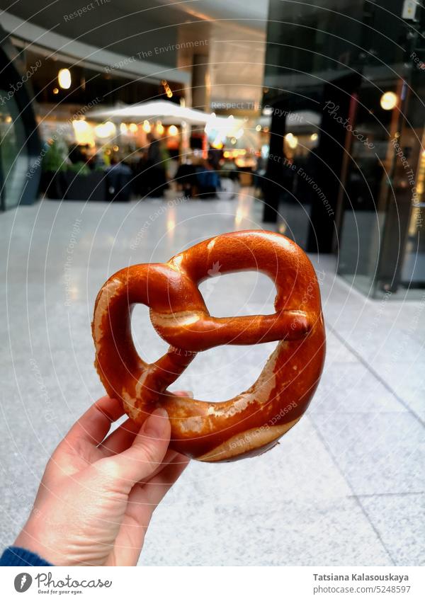 A woman's hand holds a traditional German pretzel against the backdrop of a cafe at Frankfurt Airport. Traditional German pastry. food snack bread german