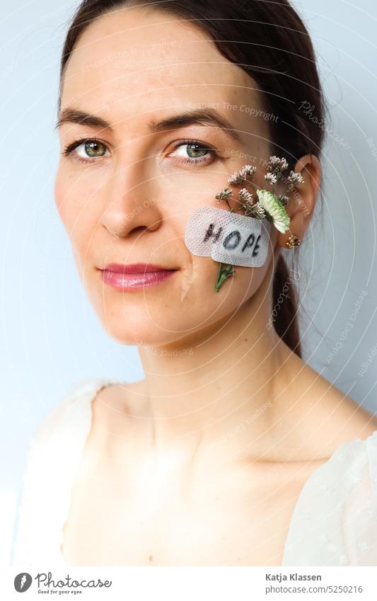 Portrait of a woman with the flowers on her cheek. The flowers are fixed with his plaster. On the plaster is written the word "Hope". portrait Young woman Cheek