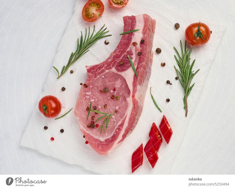 Raw pork tenderloin on the bone and spices on a white background. Portion for lunch and dinner, top view raw red rosemary meat preparation savory seasoning
