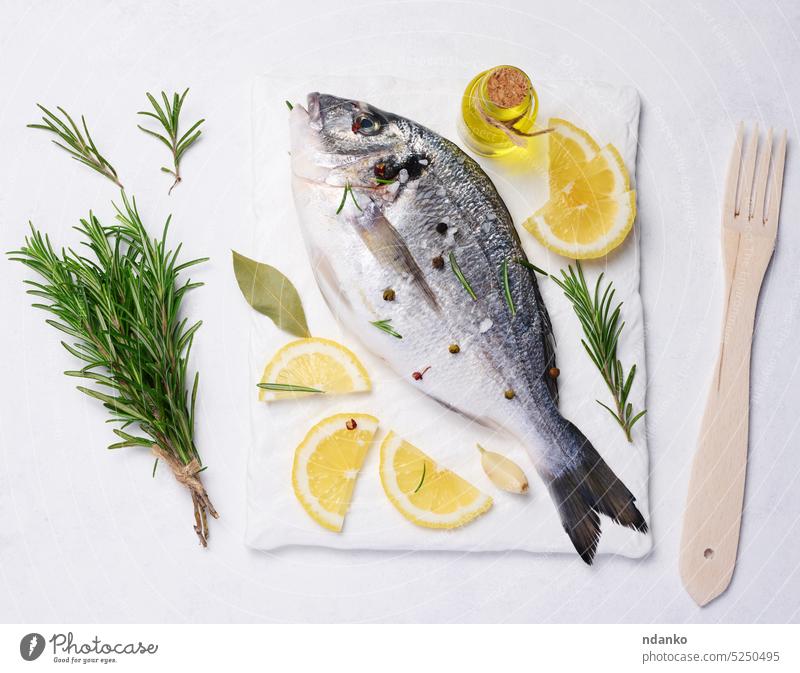 Raw whole dorado fish on white board and spices for cooking, top view on white table raw seafood rosemary salt lemon garlic parchment preparation freshness