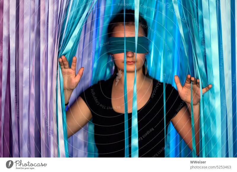 Blindfolded, the young woman feels her way out of the thicket of colorful ribbons - soon she has made it. Woman Girl youthful interconnected eyes game frisky