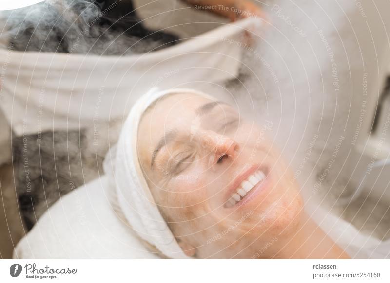 steaming the skin of the face of a happy woman before cleaning the skin in a cosmetology salon massage cream towel hand therapy facial steamer treatment