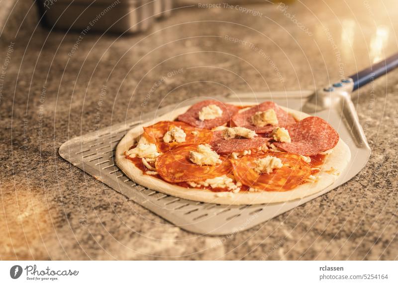 Pizza maker preparing the typical salami pizza in the italian pizzeria prepare dough raw wood fire brick oven chef cook gourmet professional work traditional