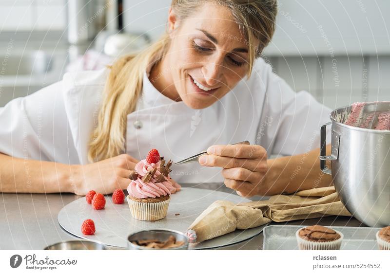 women in pastry bakery as confectioner draped pieces of chocolate on a muffin topping with tweezers icing bag pink raspberry cake cupcake birthday sugar party