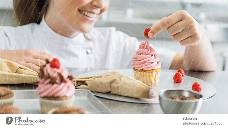Women in pastry bakery working on muffins putting a raspberry on top hand icing bag pink cake cupcake birthday sugar party candy celebration dessert food