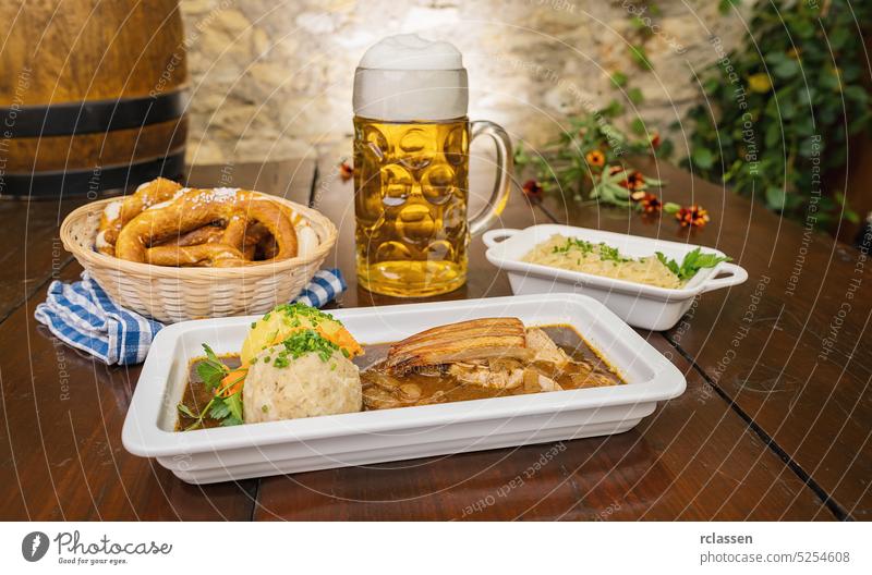 schweinskrustenbraten mit biersauce, in German cuisine, is a pork crust roast with beer sauce, with cabbage and potato dumpling, brezen and beer mug in a Bavarian beer garden or oktoberfest
