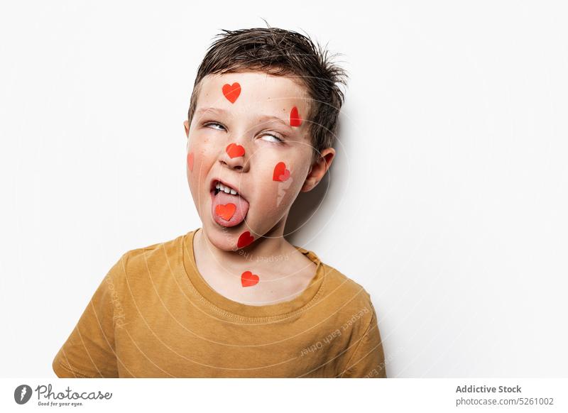 Funny boy with hearts on face show tongue funny make face roll eyes saint valentine day holiday love childhood kid playful paper childish cute adorable symbol