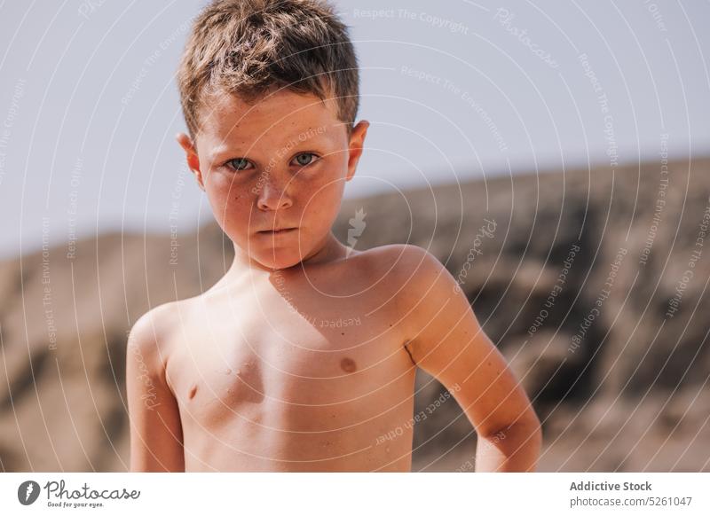 Unhappy boy standing on beach looking at camera child frown upset sea coast nature summer displease frustrate problem mood sad unhappy kid lanzarote