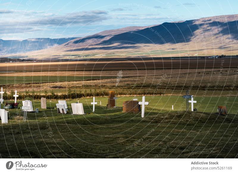 Catholic cemetery in countryside field graveyard landscape tombstone grassy gravestone valley picturesque scenery cloudy nature iceland blue sky sunlight