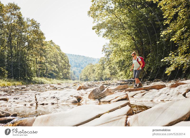 Trekking with backpack concept image. Female backpacker wearing trekking boots crossing mountain river. Woman hiking in mountains during summer trip adventure