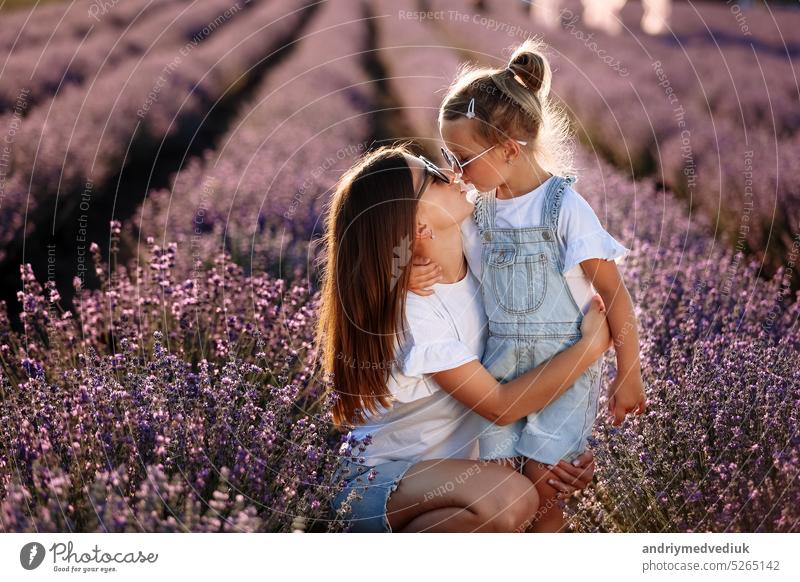 Happy family in purple lavender field. young beautiful mother and child Girl enjoy walking blooming meadow on summer day. Mom having fun with pretty daughter in nature on sunset. mothers day