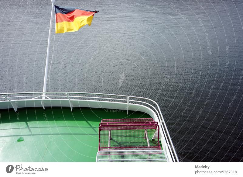 German flag in black, red and gold waving in the wind in the sunshine at the stern of an excursion boat on the Edersee near Waldeck in the district of Waldeck-Frankenberg in the German state of Hesse