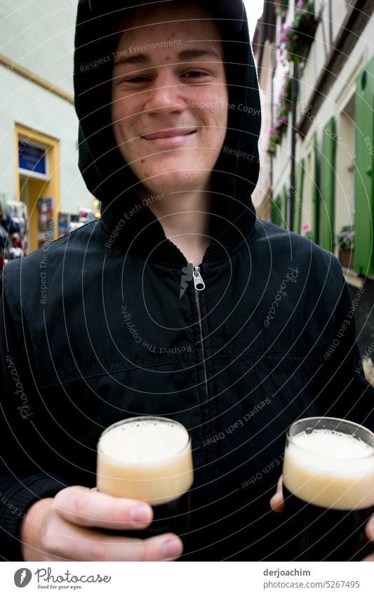 A young man is standing on the street in Bamberg with two glasses of dark beer in his hand. Beer Alcoholic drinks Drinking Glass Beverage Foam Exterior shot