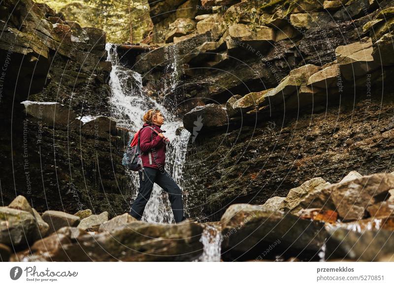 Hiking in mountains. Woman enjoying hike on sunny vacation day. Female with  backpack walking close to waterfall. Spending summer vacation close to  nature - a Royalty Free Stock Photo from Photocase