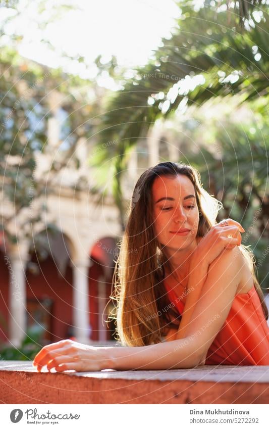 young woman in red dress looking down, smiling in the garden backlit with sunshine. summer outdoor lifestyle portrait. happy Woman Smiling Happy Joy Adults